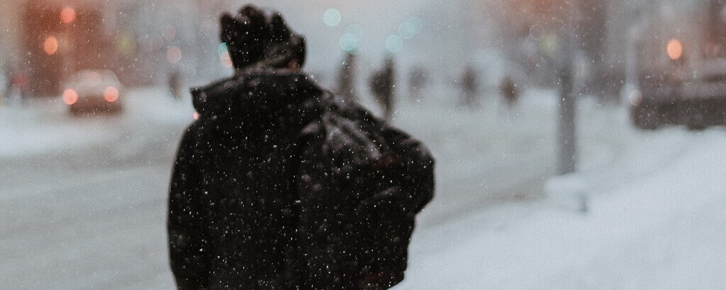 man walking in town whilst it is snowing